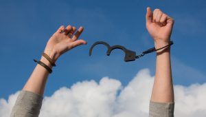 A person breaking free from handcuffs against an optimistic, blue sky background